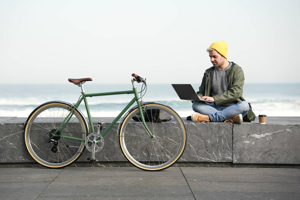 Hispanic freelancer working at the coast beside bicycle. Urban mobility and sustainability concept. - Photo, Image