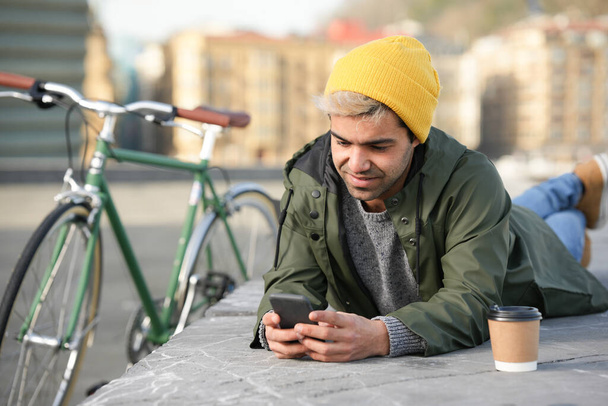 Joven hombre hispano charlando en su teléfono tendido junto a la bicicleta clásica. - Foto, imagen