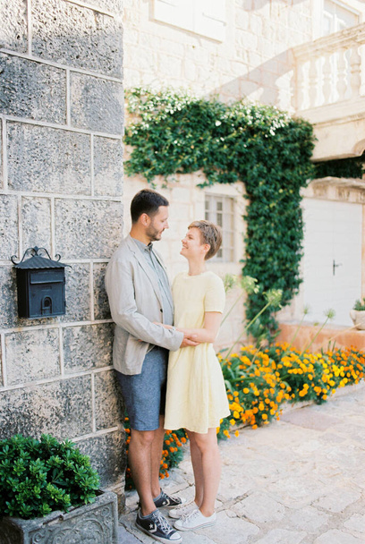 Uomo e donna sono in piedi vicino a un muro di pietra di una casa vicino aiuole fiorite - Foto, immagini