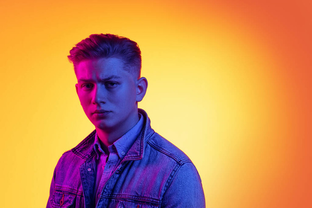 Closeup young handsome man wearing casual youth style clothes isolated on orange background in neon light, filter. Concept of emotions, beauty, fashion - 写真・画像