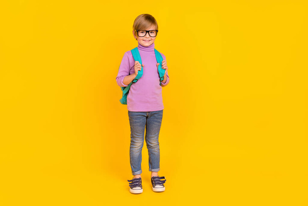 Фотографія повного розміру милого гарного маленького школяра в рюкзаку перший день в школі ізольовані на жовтому кольорі
 - Фото, зображення