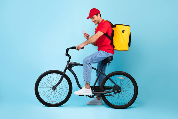 自転車の上に座っているスマートフォンを使用して宅配便,青の背景 - 写真・画像