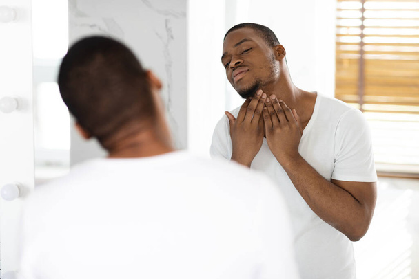 Ingegroeid haarprobleem. Portret van ongeschoren zwarte man aanraken nek met haren - Foto, afbeelding