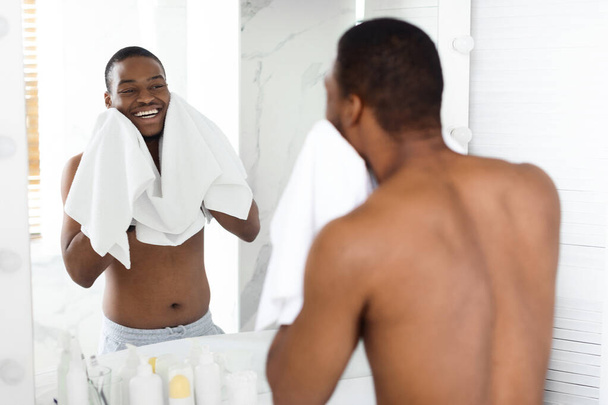 Goedemorgen Routine. gelukkig Shirless zwart jonge man vegen gezicht met handdoek - Foto, afbeelding