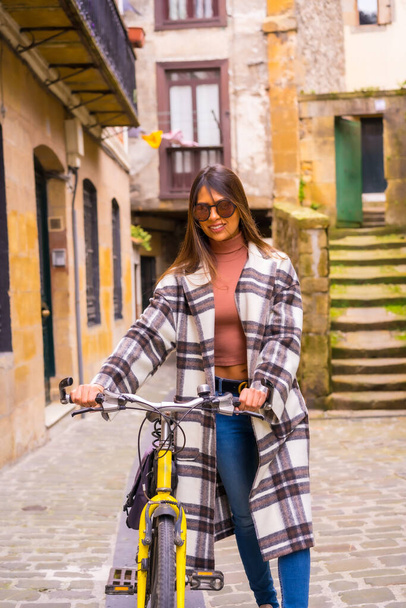 Latijnse vrouw met een zonnebril doet een fietstocht door de stad door de oude stad. Leefwijze van ecotoerisme in het voorjaar - Foto, afbeelding