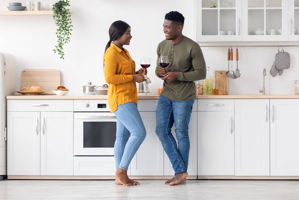 Happy Romantic African American Couple Drinking Wine And Chatting Together In Kitchen - Photo, Image