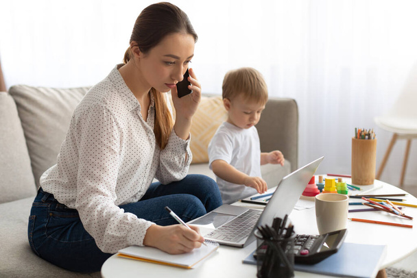 Work at maternity leave. Woman working at home and spending time with son, freelancer lady multitasking, free space - 写真・画像