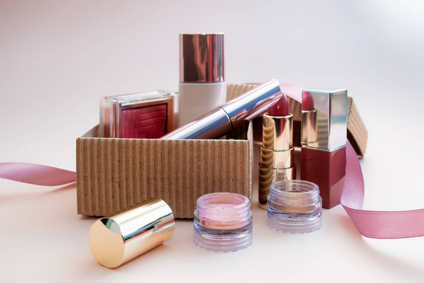 a set of cosmetics for a female face and eye makeup in a brown craft box on a pink background. photo - Fotografie, Obrázek
