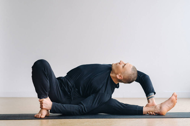 A man in black sportswear is doing Yoga, stretching in the gym. - Φωτογραφία, εικόνα