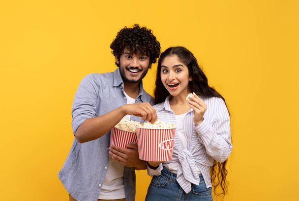 Amazing entertainment, leisure time together. Surprised indian guy and lady eating popcorn and watching movie - Photo, Image