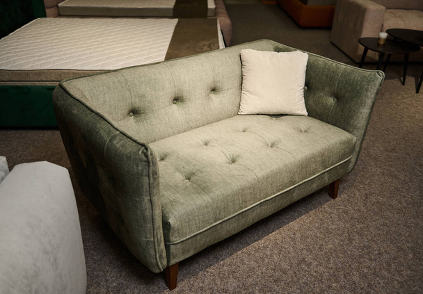 Έκθεση καναπέδων και κουβερτών με διαφορετική ποιότητα και υφή υφασμάτων στον εκθεσιακό χώρο ενός καταστήματος επίπλων. Εστίαση σε ένα πράσινο μικρό άνετο βελούδινο καναπέ, εμφανίζεται προς πώληση - Φωτογραφία, εικόνα