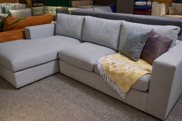Сучасний м'який затишний сірий диван зі стильними велюровими подушками і жовтим ковдрою, виставлений на продаж в демонстраційному залі м'якого меблевого магазину для домашніх меблів. Дизайн інтер'єру та оздоблення будинку
 - Фото, зображення