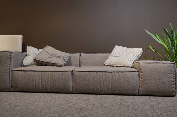 Exposición de mobiliario tapizado con diferentes tejidos de calidad y textura en el showroom. Hermoso sofá grande cómodo con almohadas contra fondo de pared marrón - Foto, imagen