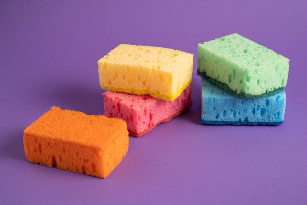 Esponjas limpiadoras de cocina. Esponjas multicolores para limpiar. Esponjas de color sobre fondo púrpura. Esponja exfoliante - Foto, imagen