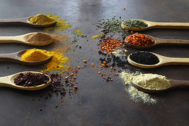 Different kind of spices on a black stone. Oriental spices in spoons, red peppers, curry powder, cinnamon powder, mint powder, colorful peppers. Flat lay, top view. - Photo, Image