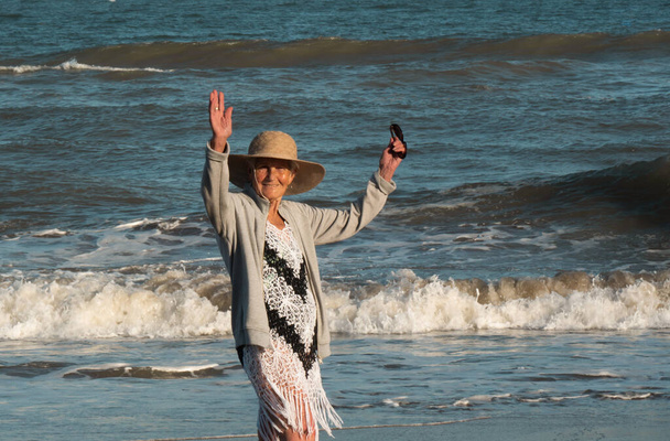 a lady walking on the beach with her black and white thread dress and her gray jumpsuit. He is happy and smiles in the photo. raise your arms with joy. - Photo, Image