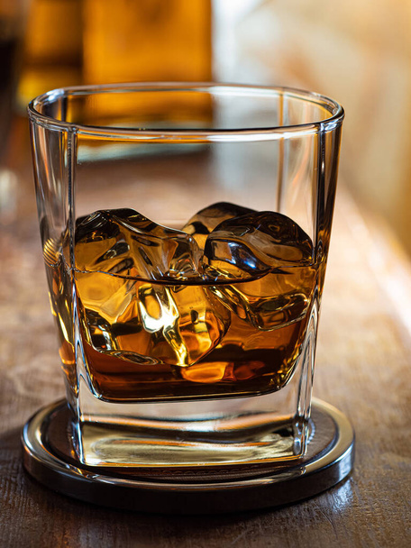 Glass of whisky on the rocks on a wooden bar top with bottles in the background - 写真・画像