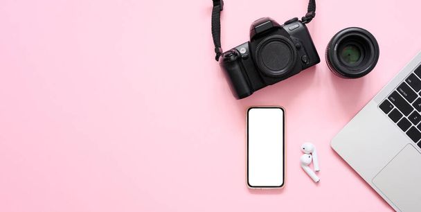 Kamera, čočka, notebook a smartphone s bílým displejem na růžovém pozadí. Fotografova pracoviště. Plocha, kopírovací prostor. - Fotografie, Obrázek