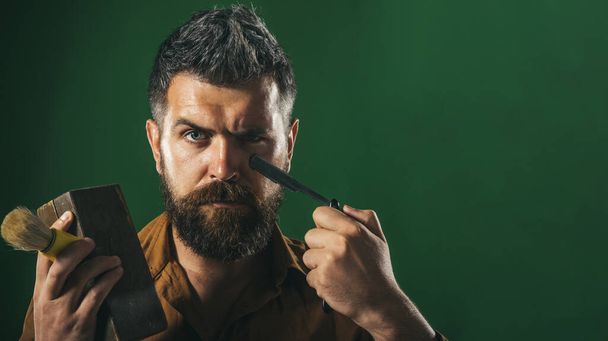 Szakállas férfi, egyenes borotvával, fa koporsóval, borotválkozó kefével a kezében. Borbélyüzlet reklámozása. - Fotó, kép