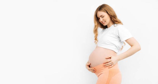 Pregnant happy beautiful woman touches her belly. Pregnant mom caressing her belly and smiling close up. Healthy pregnancy concept, pregnant woman on isolated white background - Foto, imagen