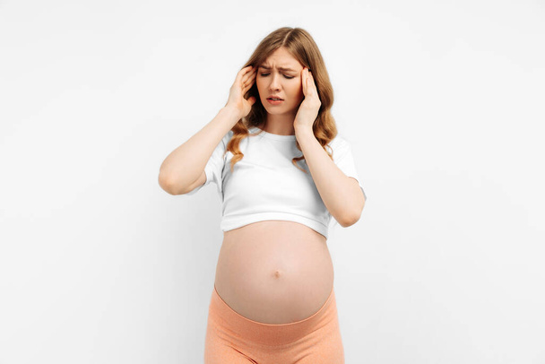 Portrait of a beautiful young pregnant woman suffering from a headache on a white background. headache due to stress, suffers from migraine. - Valokuva, kuva