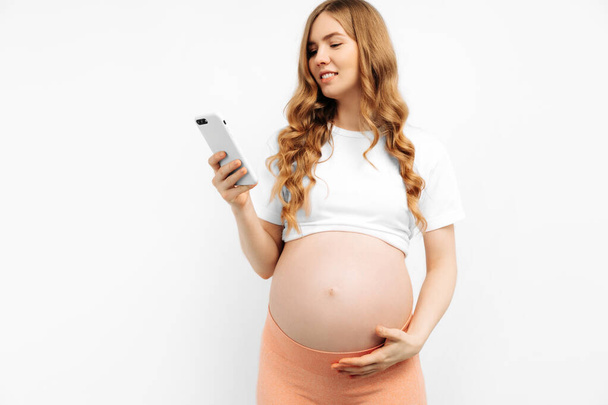 pregnant woman using mobile phone on white background. A pregnant woman is holding a smartphone. Pregnancy, motherhood, technology, expectation concept - close-up of pregnant woman with smartphone - Photo, Image