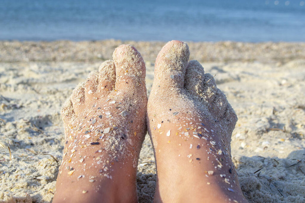 Dos pies desnudos de mujer caucásica manchada de arena con roca de concha en el mar arenoso - Foto, Imagen