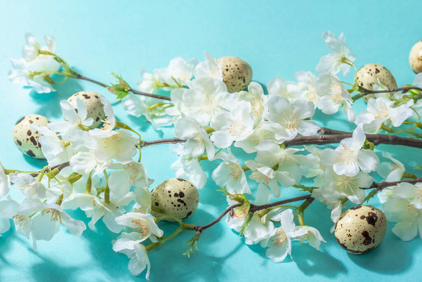 幸せなイースターのお祝いのフラットは、桜と卵を咲かせます。春休みの伝統的なシンボルです。流行のハードライトダークシャドウ、繊細な青の背景、トップビュー、コピースペース、フラットレイアウト - 写真・画像