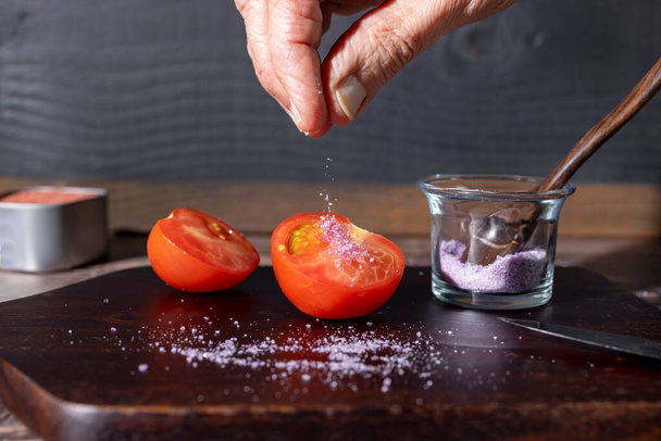 Chef salando un tomate a la mitad en una tabla de cortar madera - Foto, imagen