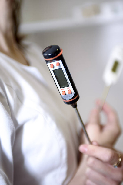 Медицинский работник держит в руках термометр для изготовления кремов и других косметических средств. - Фото, изображение