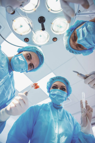 Chirurdzy zespołowi wykonują operację przy użyciu przyrządów medycznych, w nowoczesnej sali operacyjnej, widok z dołu - Zdjęcie, obraz