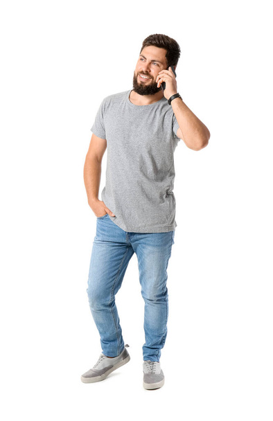 Красивый мужчина в серой футболке разговаривает по мобильному телефону на белом фоне - Фото, изображение