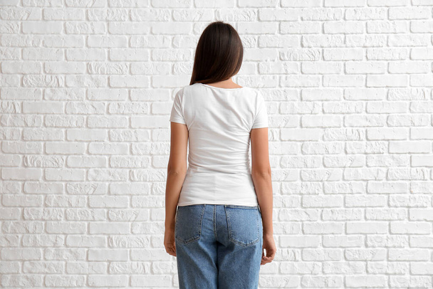 Молодая женщина в пустой футболке на белом кирпичном фоне, вид сзади - Фото, изображение