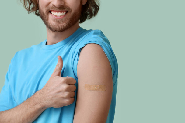 Jongeman met toegepaste medische patch met duim-up op kleur achtergrond - Foto, afbeelding