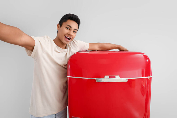 Giovane uomo afro-americano prendere selfie con elegante frigorifero rosso su sfondo chiaro - Foto, immagini