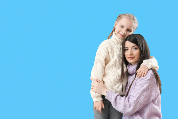 Niña y su madre en suéteres cálidos abrazándose sobre fondo azul - Foto, Imagen