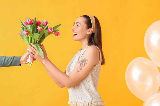 Happy young woman with bouquet of tulips from man on yellow background. International Women's Day - Photo, Image