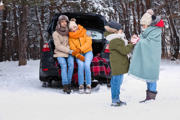 Niños felices con sus padres y coche en el bosque en el día de invierno nevado - Foto, imagen