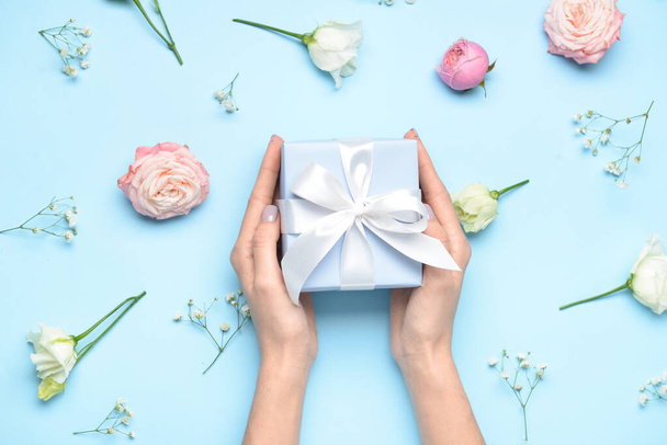 Female hands with gift box for International Women's Day and beautiful flowers on color background, closeup - Fotoğraf, Görsel