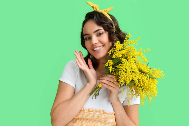 Belle jeune femme avec bouquet de fleurs de mimosa sur fond vert - Photo, image