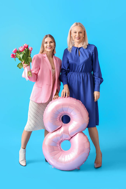 Зріла жінка з донькою, тюльпаном і кулькою на синьому фоні. Міжнародний жіночий день - Фото, зображення