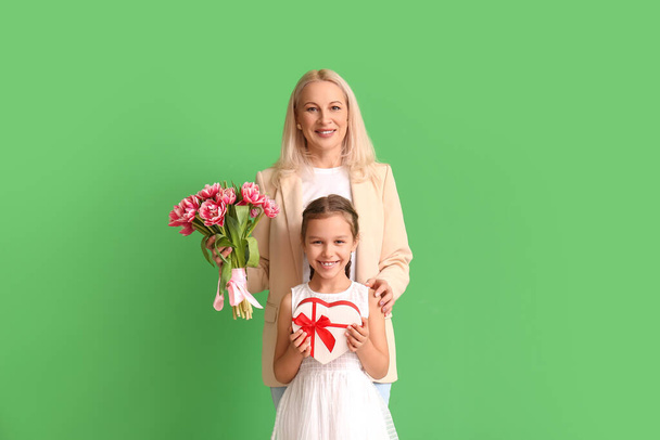 Mature woman with her little granddaughter and gifts on green background. International Women's Day - Foto, Bild