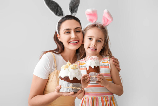 Little girl and her mother in bunny ears with Easter cakes on light background - Fotoğraf, Görsel