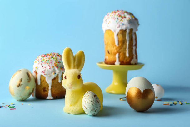 Mavi arka planda boyalı yumurta ve kekleri olan şirin Paskalya tavşanı. - Fotoğraf, Görsel