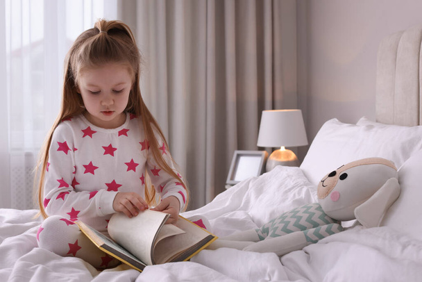 Cute little girl reading book on bed at home - Fotoğraf, Görsel