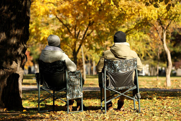 Couple sitting in camping chairs outdoors on autumn sunny day, back view - Fotó, kép