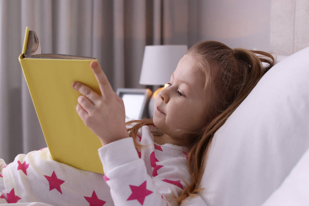 Cute little girl reading book on bed at home - Photo, Image