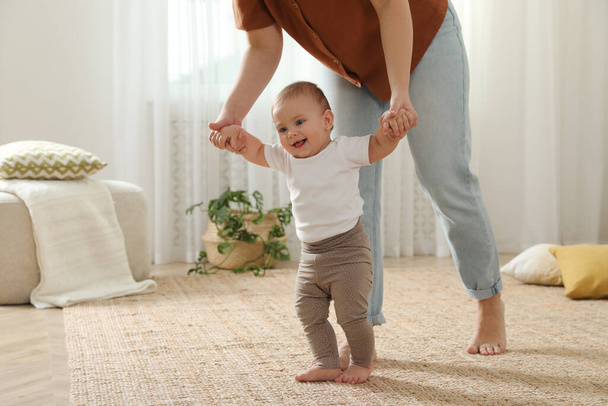 Mother supporting her baby daughter while she learning to walk at home - Foto, Bild