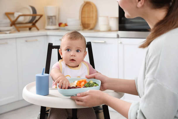 Mother feeding her cute little baby in kitchen - Photo, image