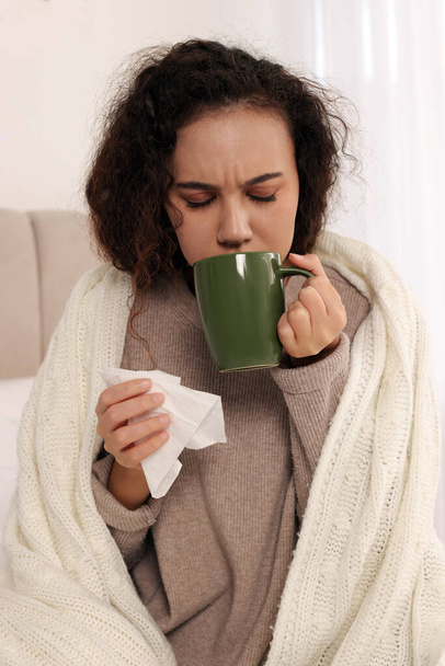 Sick African American woman with tissue and cup of drink in bed at home - Photo, image